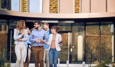 Geniş bir grup genç iş adamı binanın dışında yürüyor.