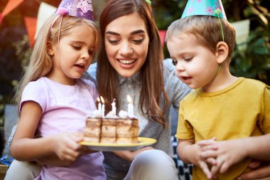 Anneleriyle birlikte mum yakmış doğum günü pastasını izleyen çocuklar.