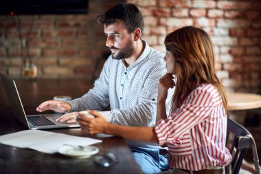 Kafkasyalı genç bir çift kafenin önünde dizüstü bilgisayarla iş fikirleri hakkında konuşuyor.