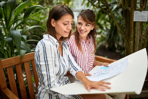 两名高加索女性景观设计师坐在植物园的木制长椅上 观摩植物园布置的草图设计 — 图库照片