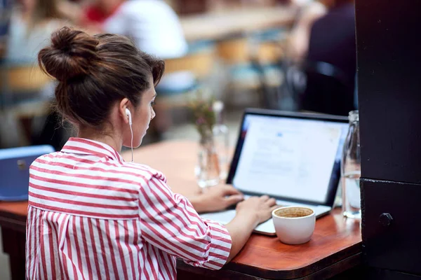 Junge Frau Tippt Auf Ihrem Laptop Mit Kopfhörern Den Ohren — Stockfoto