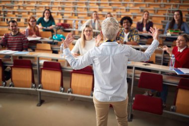 Yaşlı kadın profesör, öğrencinin sorularını amfi tiyatroda cevaplıyor.