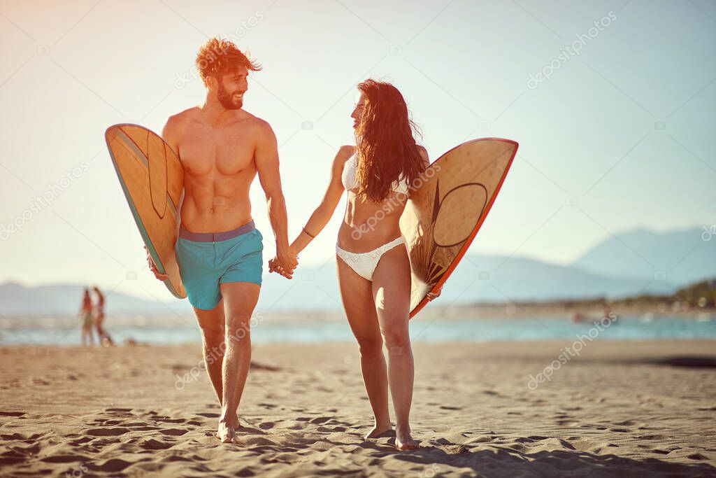 Sporty smiling couple having fun going to surf together at sunset.