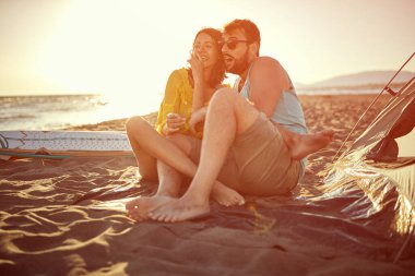 Gün batımında sahilde kamp yapan gülümseyen genç arkadaşlar..