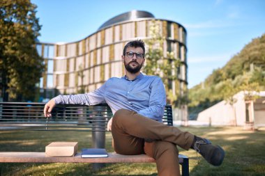 Şehirdeki bir bankta oturan ciddi genç işadamı. İnsanlar molada dışarıda bankta oturuyor..