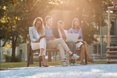 Bir grup genç iş adamı parktaki bankta cep telefonları, laptopları ve tabletleriyle gülüyorlar. Mola, işten dur.