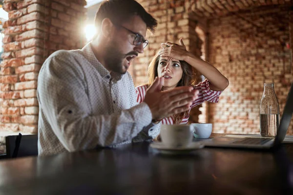 年轻的高加索夫妇看着面前的笔记本电脑 听到坏消息 犯了错误 在咖啡店喝咖啡 — 图库照片