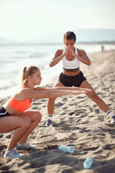 Dos Jóvenes Caucásicas Haciendo Sentadillas Ropa Deportiva Playa Arena Junto —  Fotos de Stock