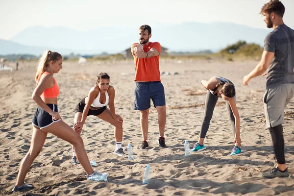 由两名男子和三名女子组成的高加索人小组进行伸展运动 准备在沙滩上进行锻炼 — 图库照片
