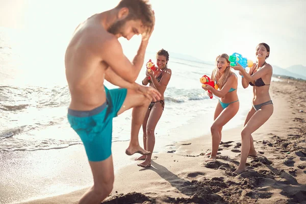 3人のセクシーな女性が砂のビーチに水銃でベアディ男を振りかけ — ストック写真