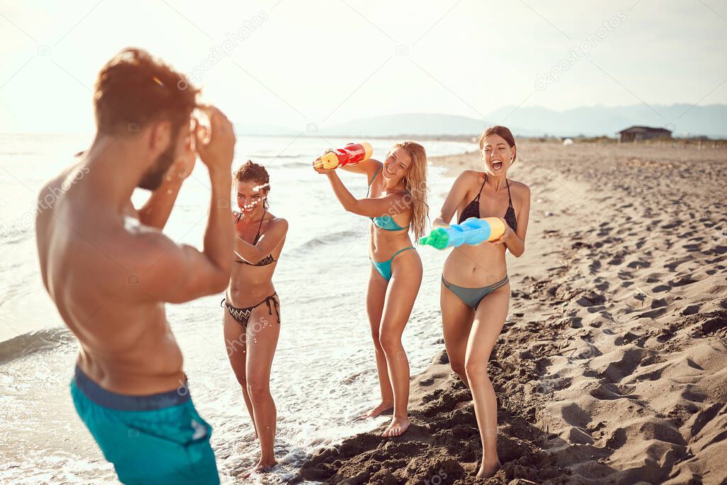 women sprinkle beardy guy with water guns on sandy beach