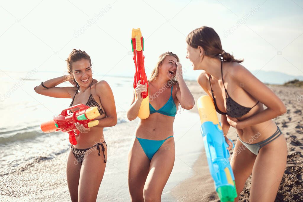 three women having fun with water guns on sandy beach