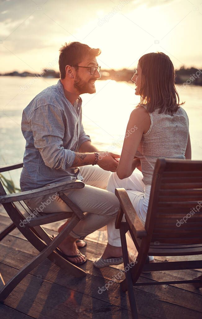 young caucasian couple sitting by the river, holding hands, talking, smiling