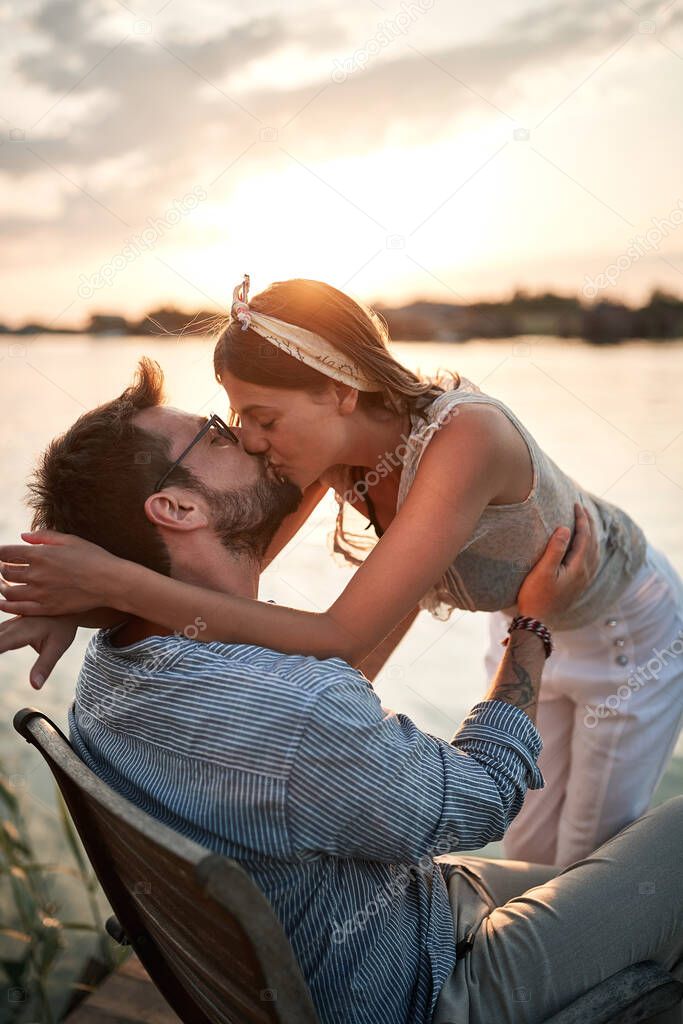 close up of young beautiful  female kissing a man on the riverside at sunset