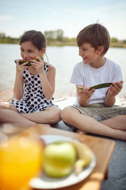 Tatlı kız ve oğlan iskelede taze karpuz yiyorlar. Çocuklar gölde birlikte eğleniyorlar.. 