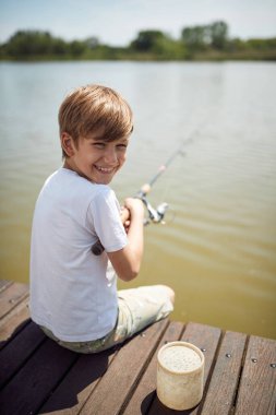 Gülümseyen çocuk gölde balık tutarken eğleniyor. Tatilde eğleniyor..