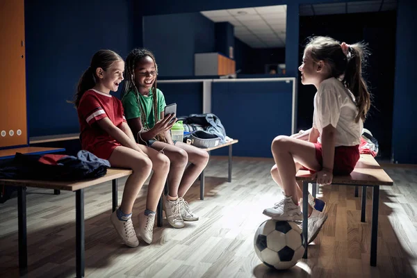 Smiling girls sitting in a changing room and talking.Girl child with soccer ball in changing room.