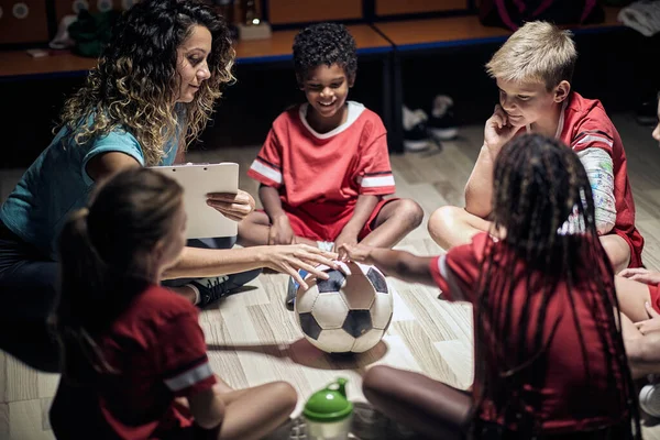 woman coach in circle in locker room with her pupil soccer sport team.