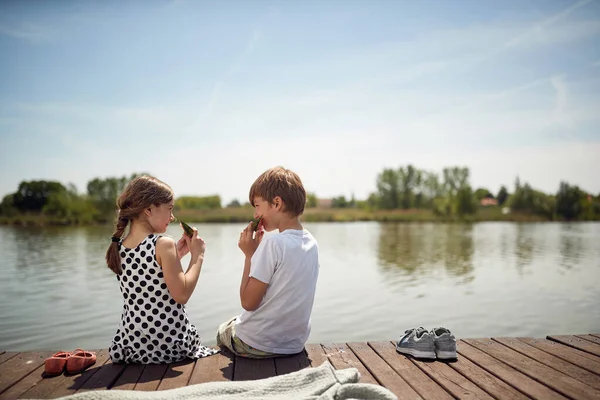 池の近くの木で子供たちを笑顔新鮮なスイカを食べる — ストック写真