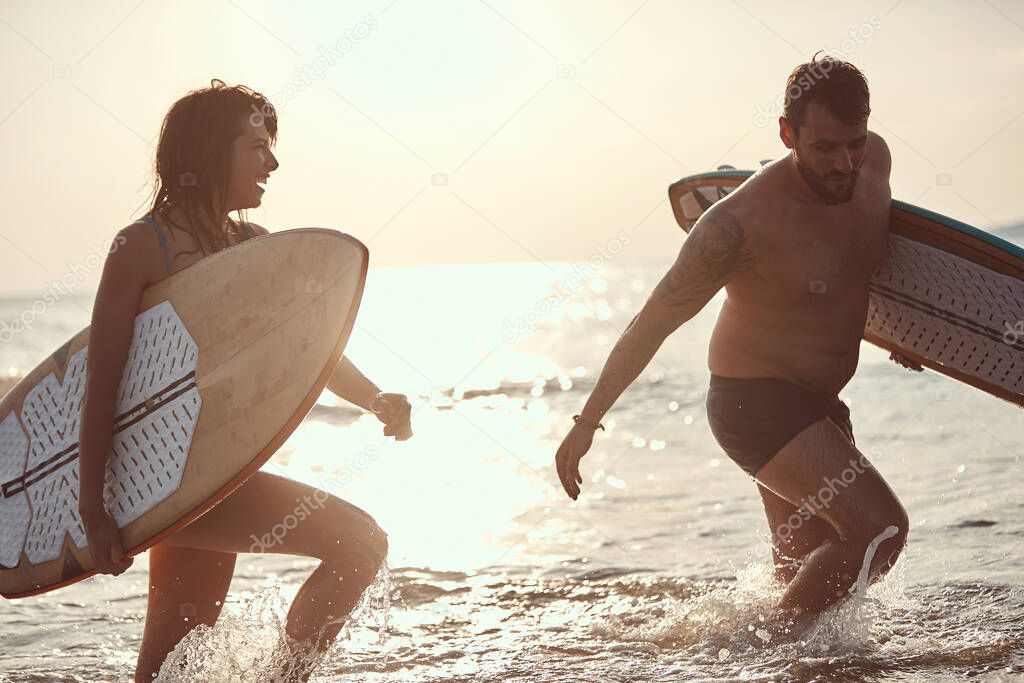 young caucasian couple getting out of the water, smiling, holding surfboards