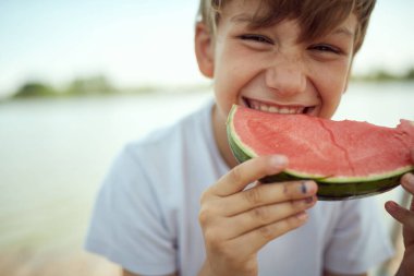 Genç bir çocuk sıcak bir günde karpuz yiyor