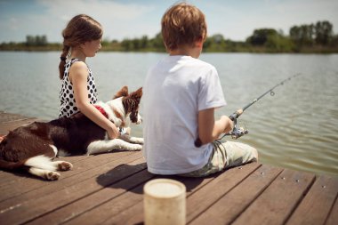 Erkek ve kız kardeşler güneşli bir günde köpekleriyle balık tutmaktan zevk alırlar.