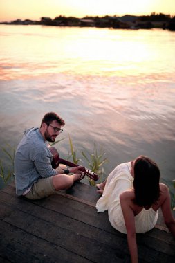 Romantik çift güzel günbatımında nehirde gitar çalıyor..