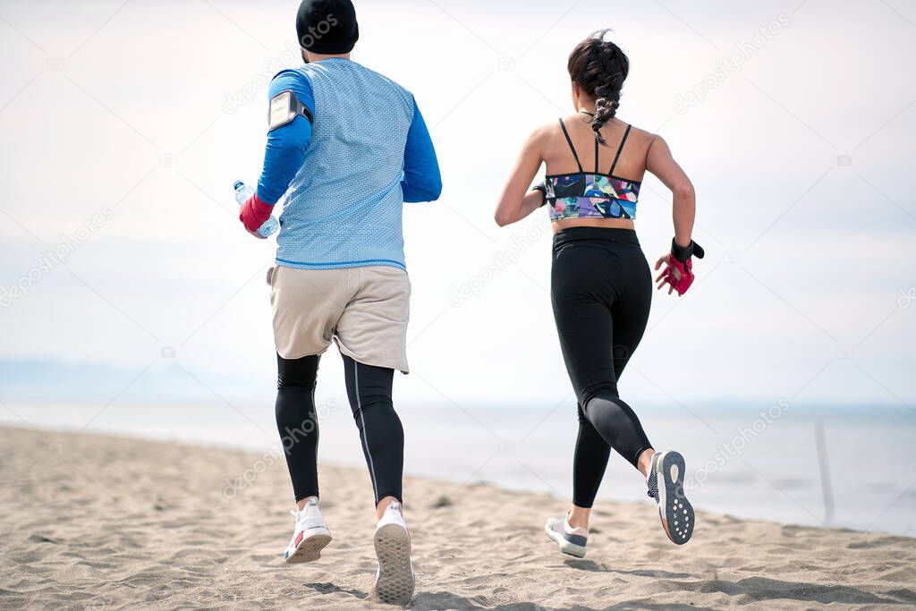 Fitness young man and woman  running along beach together.