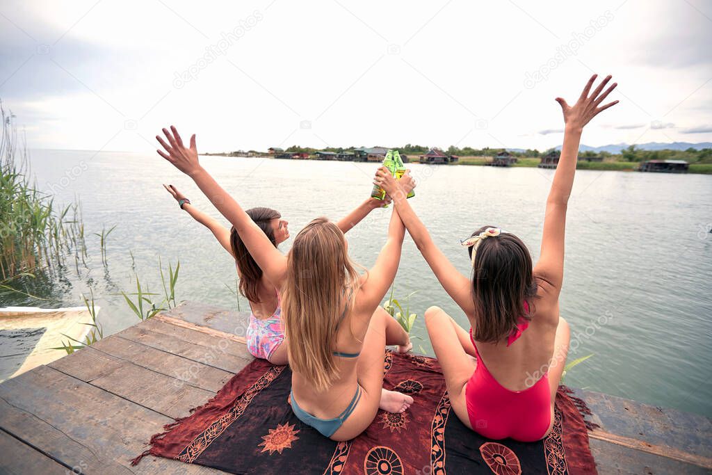 Young  smiling women in swimsuit have fun on the dock on lake and drink beer.