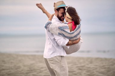 Beyaz sakallı adam sahilde kız arkadaşını kollarında taşıyor.