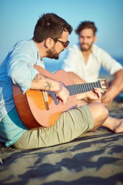 Çocuklar sahilde takılıp gitar çalıyorlar.