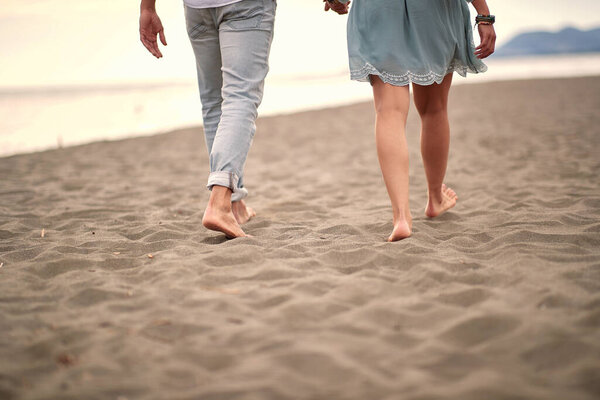 cropped image of  young caucasian couple in casual barefoot walk on sandy beach