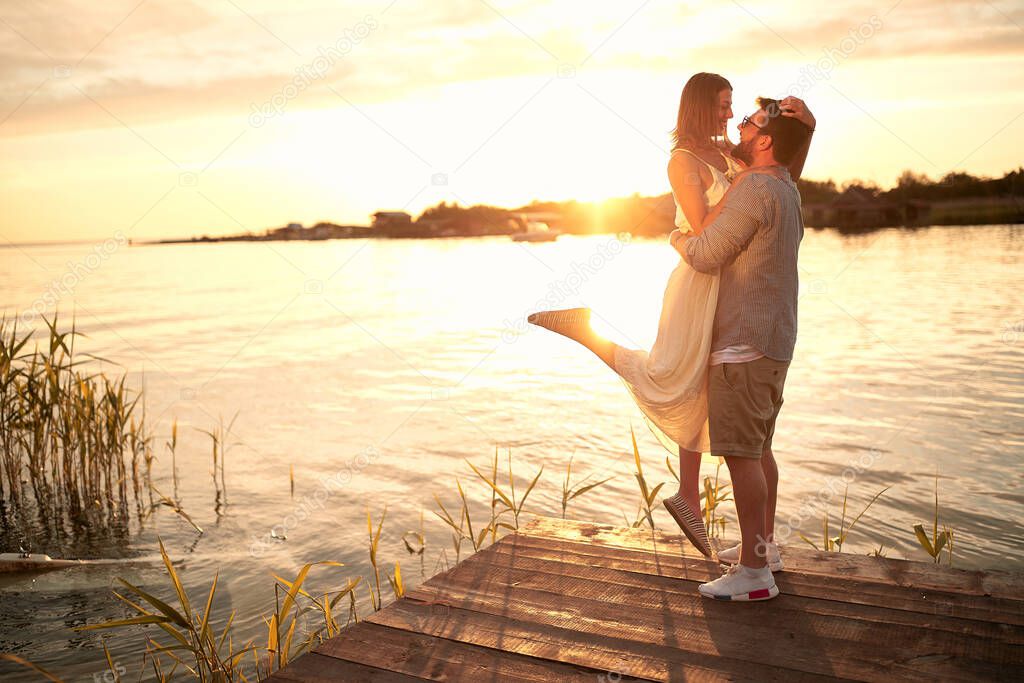 caucasian beardy guy holding up his girlfriend at sunset by the river