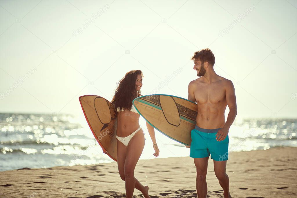 Young attractive couple sourfing together on the beach