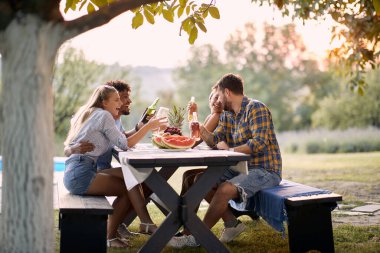 Bir grup çok ırklı genç arkadaş dışarıda eğleniyor, konuşuyor ve gülüyorlar.