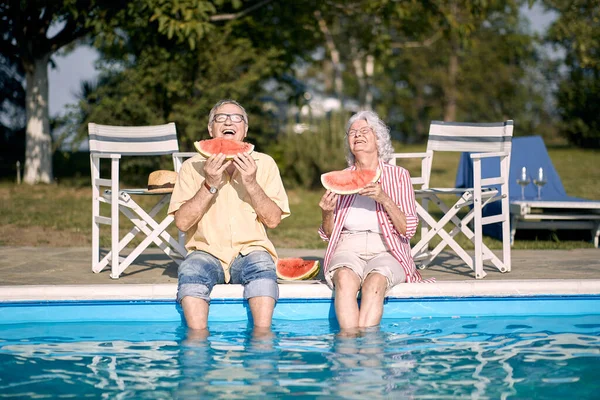 Elderly  couple  eating watermelon by the pool.Happy man and woman enjoy on summer holiday .