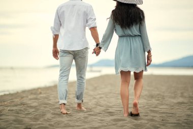 Genç aşık bir çift güneşli bir havada sahilde yürüyor.