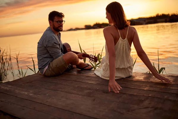 年轻夫妇带着吉他和美丽的天气在湖上欣赏日落 — 图库照片