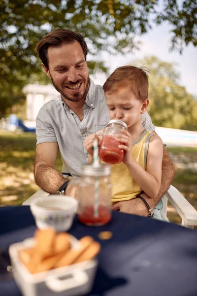 Smiling father with  son sitting at table outdoor and  enjoying together.