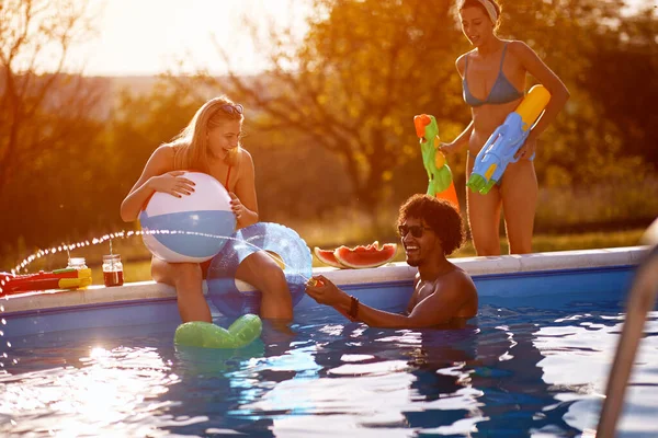 プールで水鉄砲遊びをする仲間幸せな若者はプールで夏休みを楽しむ — ストック写真