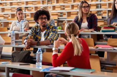 Erkek öğrenci, amfitiyatroda meslektaşlarıyla oturuyor.