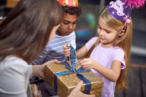 caucasian girl unwrapping birthday present from young adult female brunette with afro-american cute little boy watching
