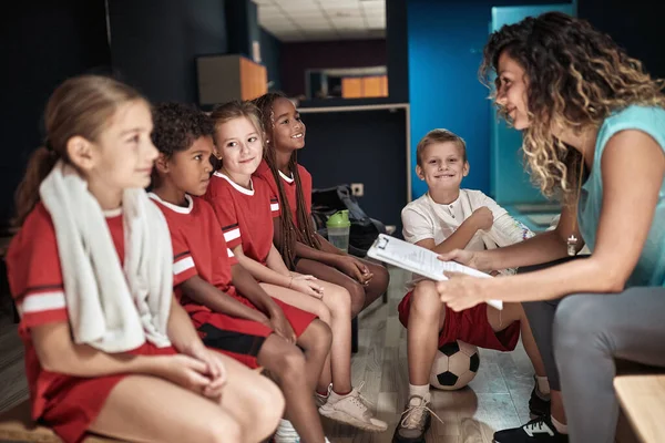 Kid's soccer team and their female coach in a locker room preparing for a training