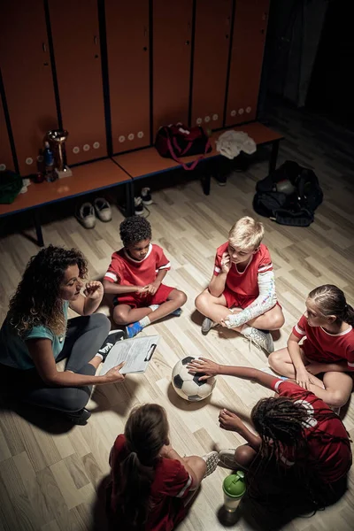 Kid's soccer team and their female coach made a relaxed atmosphere in a locker room  before training