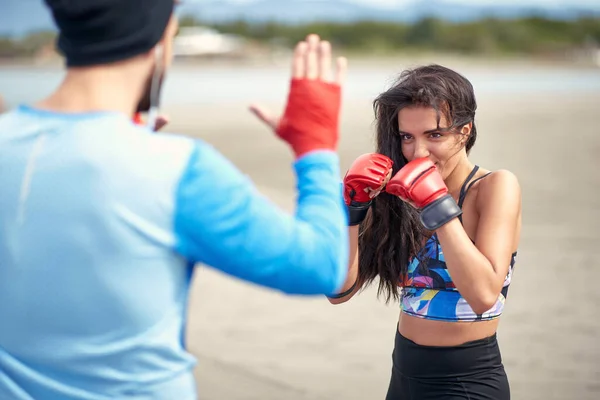 年轻的女拳击手和她的教练在海滩上接受训练 — 图库照片