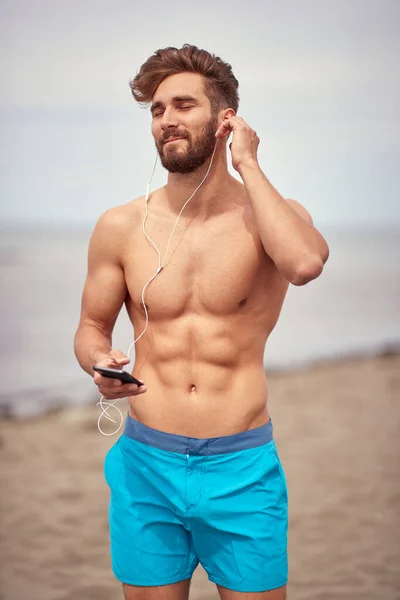 Kumsaldaki Genç Yakışıklı Adam Güneşli Bir Havada Akıllı Telefonuyla Müzik — Stok fotoğraf