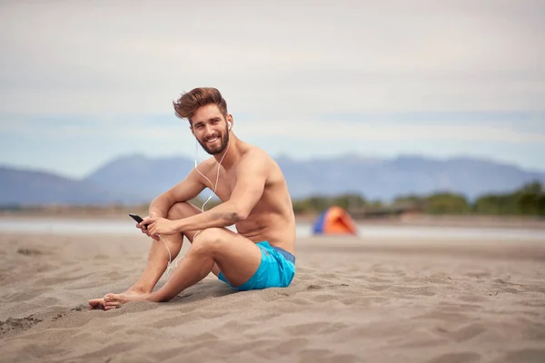 Młody Przystojny Mężczyzna Siedzi Plaży Słucha Muzyki Słoneczną Pogodę — Zdjęcie stockowe