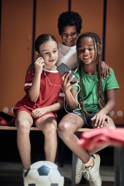 Küçük bir futbolcu soyunma odasında arkadaşlarına cep telefonu içeriğini gösteriyor.