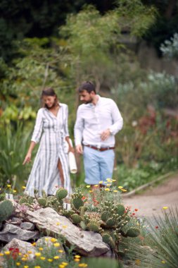 Genç bir kadın rehber ve genç bir erkek ziyaretçi botanik bahçesindeki güzel bitkilerin arasında yürüyorlar.