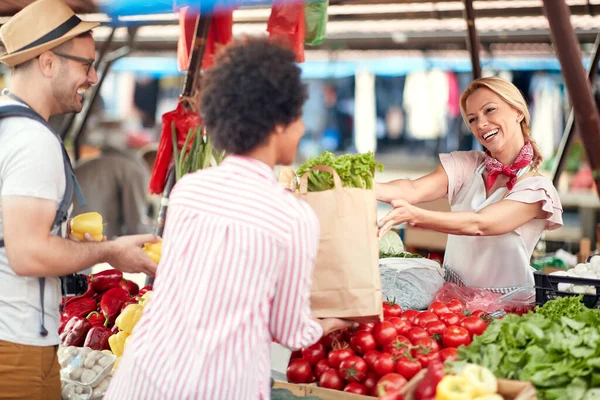 売り手の女性は 緑の市場や農家の市場の屋台で新鮮な有機野菜や果物を提供しています 若いバイヤーは食料品の健康な食糧のためのプロダクトを選び 健康的な食事 ライフスタイルのためのすべて — ストック写真